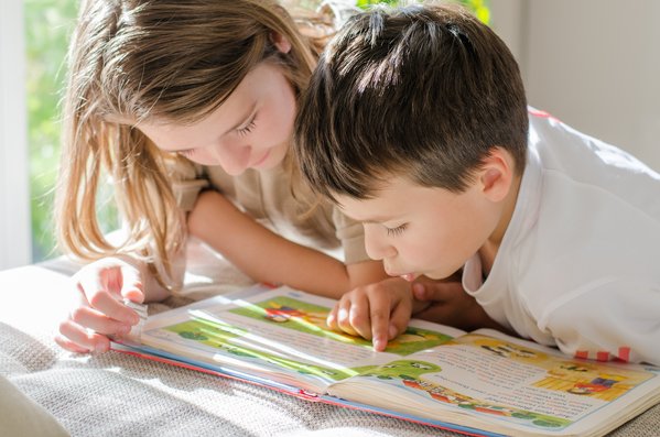 Ein Kind hilft einem jüngeren Kind zu lesen