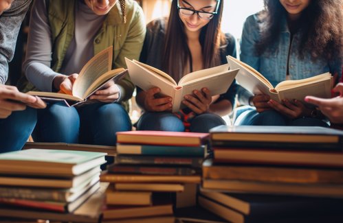 ©Adobe Stock Drei Stapel Bücher im Vordergrund. Dahinter 5 Kinder, die lesen.