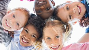 Kinder im Alter von ungefähr sechs Jahren stehen im Kreis, halten sich an den Armen und lachen in die Kamera