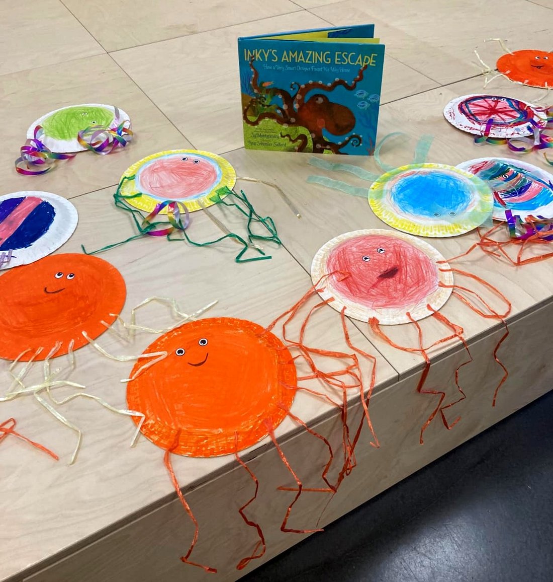 Bild mit orangem und rotem Oktopu und einem Bilderbuch auf einem Tisch.