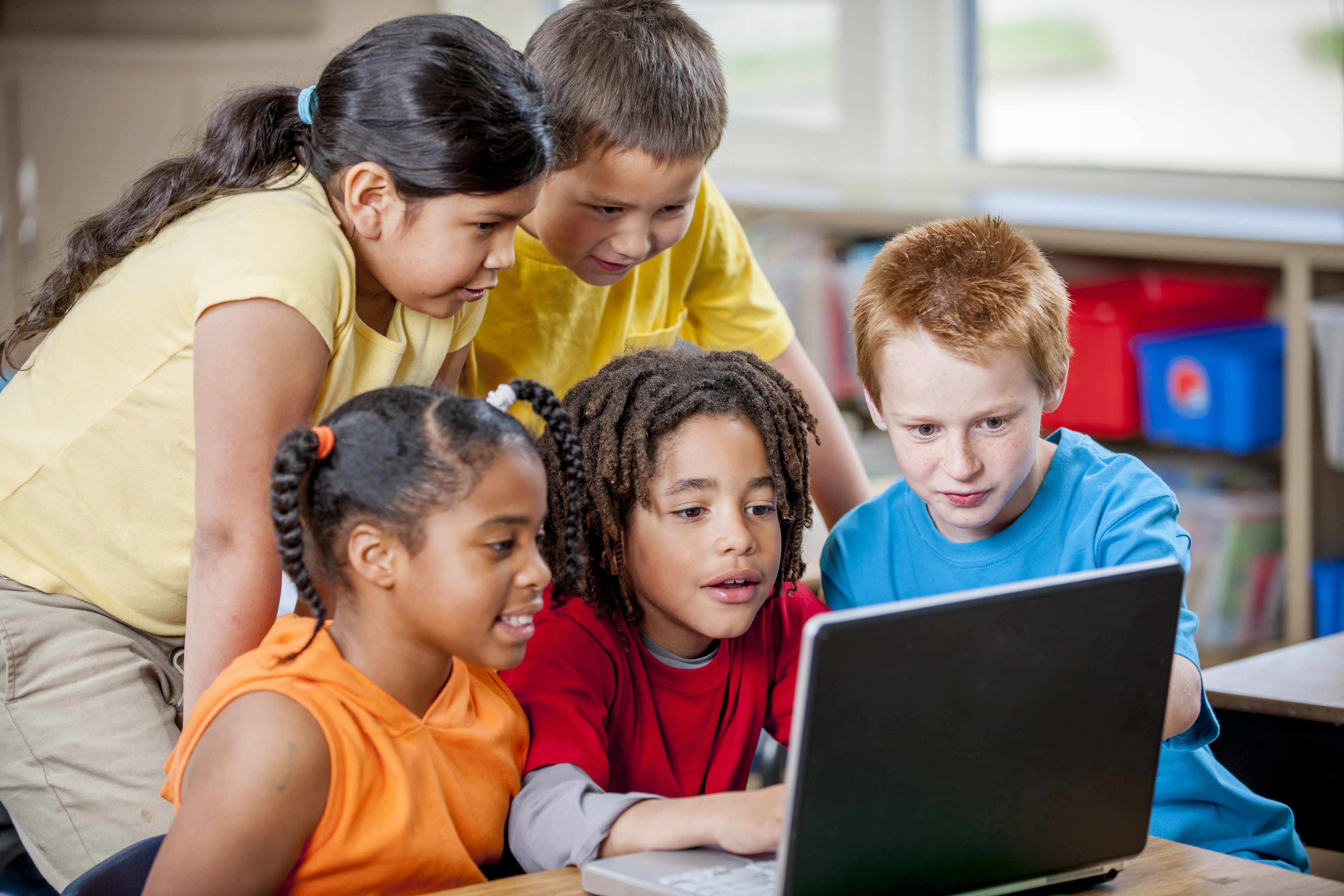 ©Adobe Stock Das Bild zeigt eine Gruppe von fünf Kindern, die um einen Laptop versammelt sind. Sie schauen gemeinsam gespannt auf den Bildschirm, während sie offensichtlich etwas Interessantes betrachten oder lernen. Die Szene spielt sich in einem hellen Raum ab, vermutlich in einem Klassenzimmer oder einer Lernumgebung.